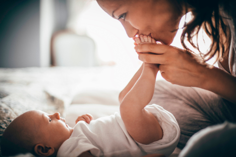 Mum leaning over baby kissing feet